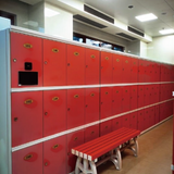 Tali Sport red plastic locker room bench with white legs placed in front of matching red lockers in a gym setting 