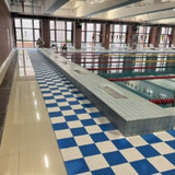 Tali Sport modular blue and white anti-slip PVC floor tiles installed around an indoor swimming pool deck 